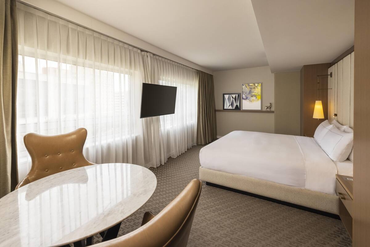 A hotel room with a bed, a TV, a dining table, and a chair.