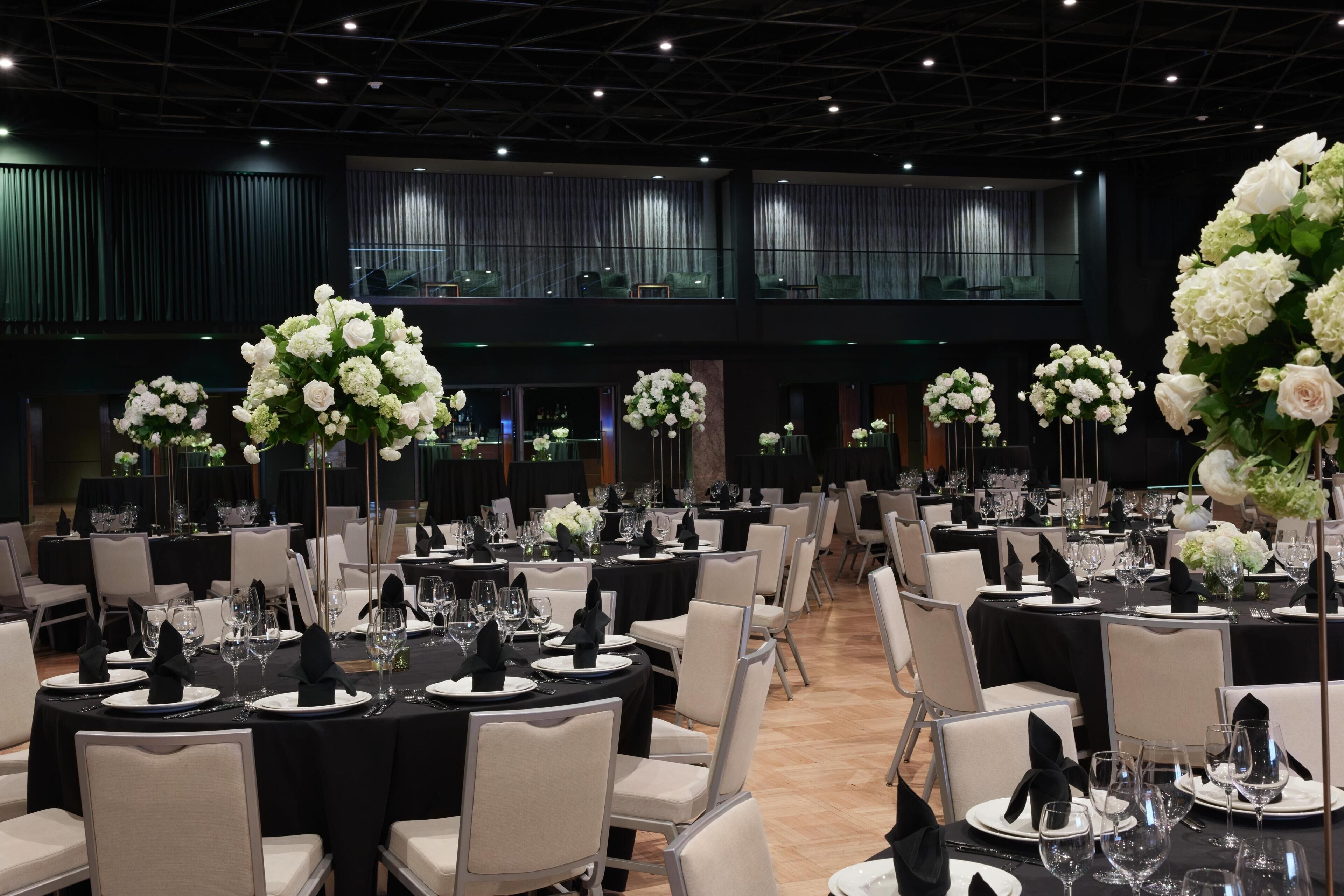 A banquet hall with round tables, black tablecloths, and white floral centerpieces.