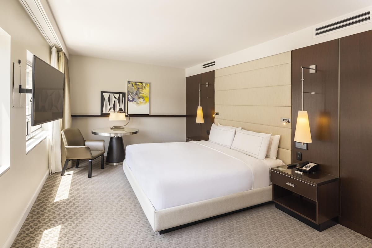 A hotel room with a large bed, a desk, a chair, a TV, and artwork on the walls.