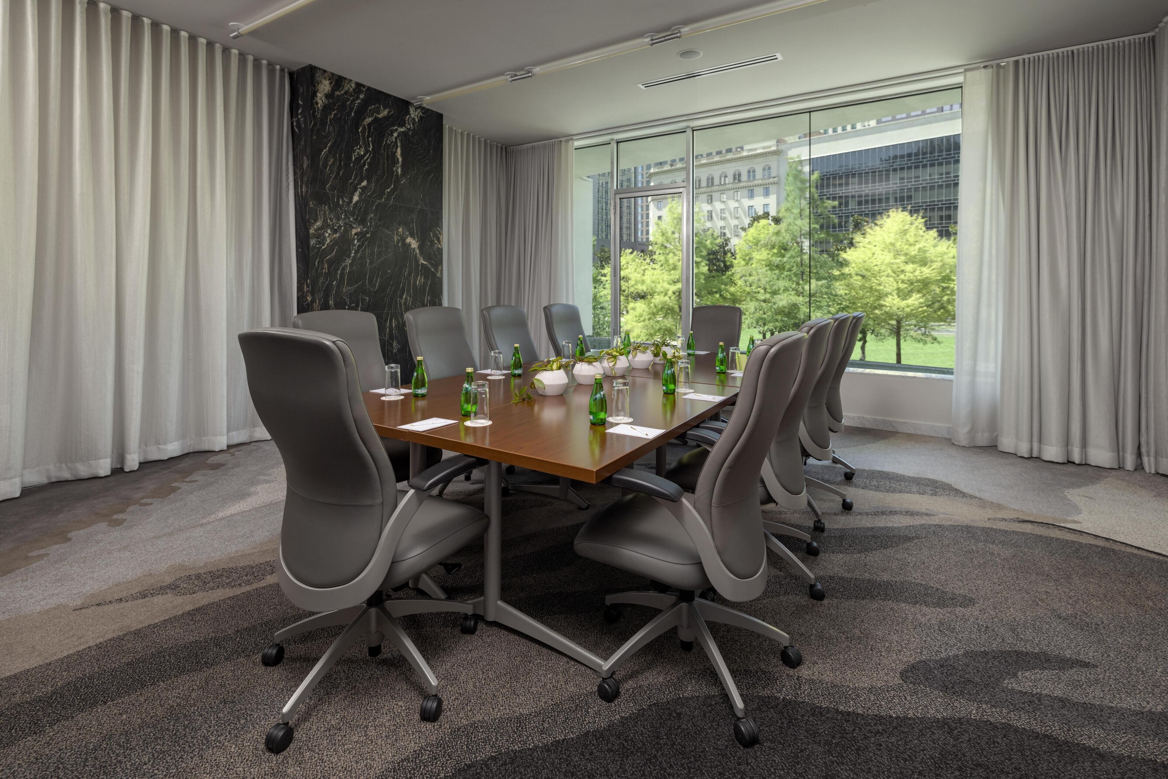 A conference room with a large table, grey chairs, and a view of a building through large windows.