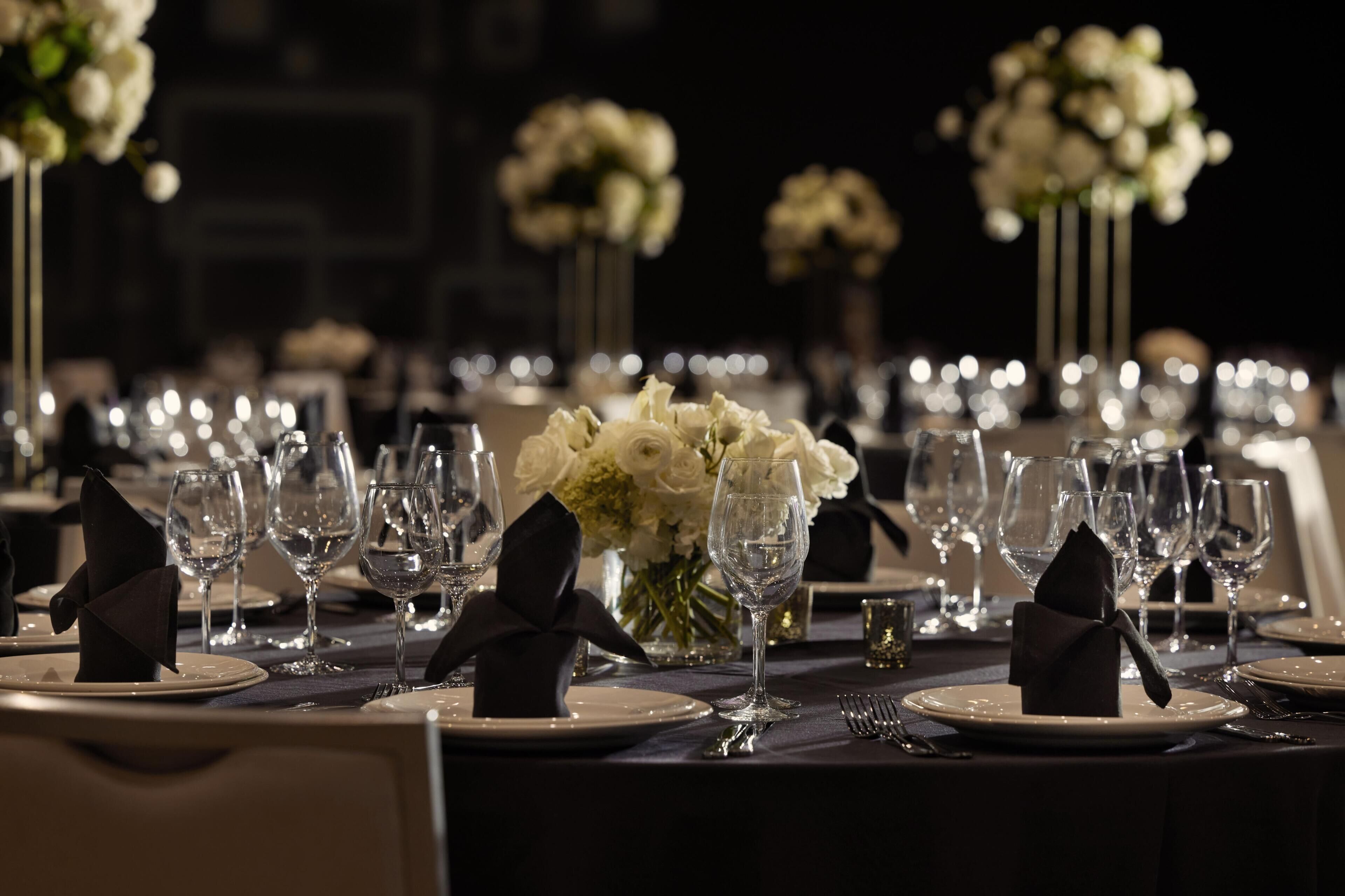 A formal dining table set with white plates, clear glasses, and black napkins.