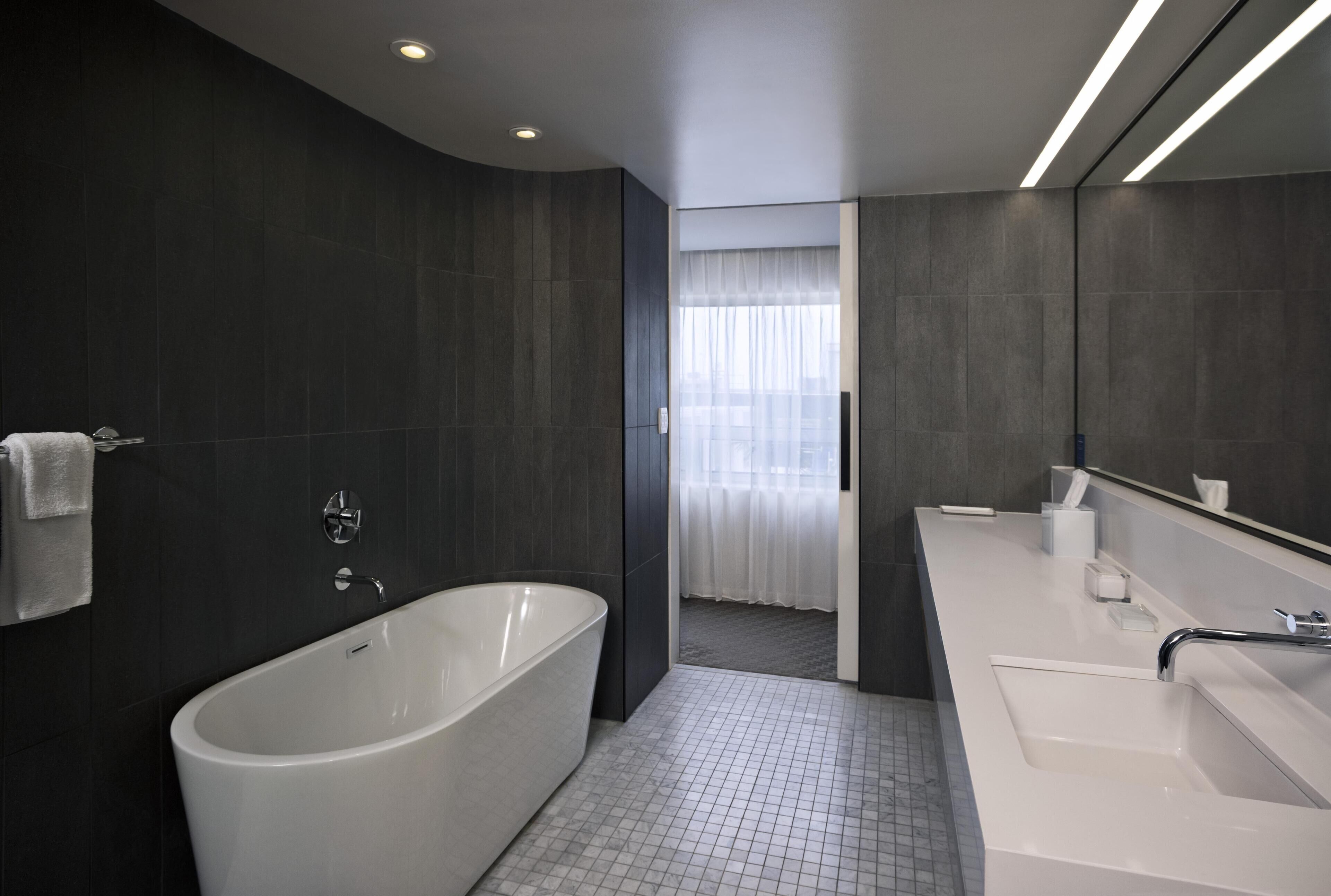 A modern bathroom with a freestanding bathtub, a large mirror, and a white sink.