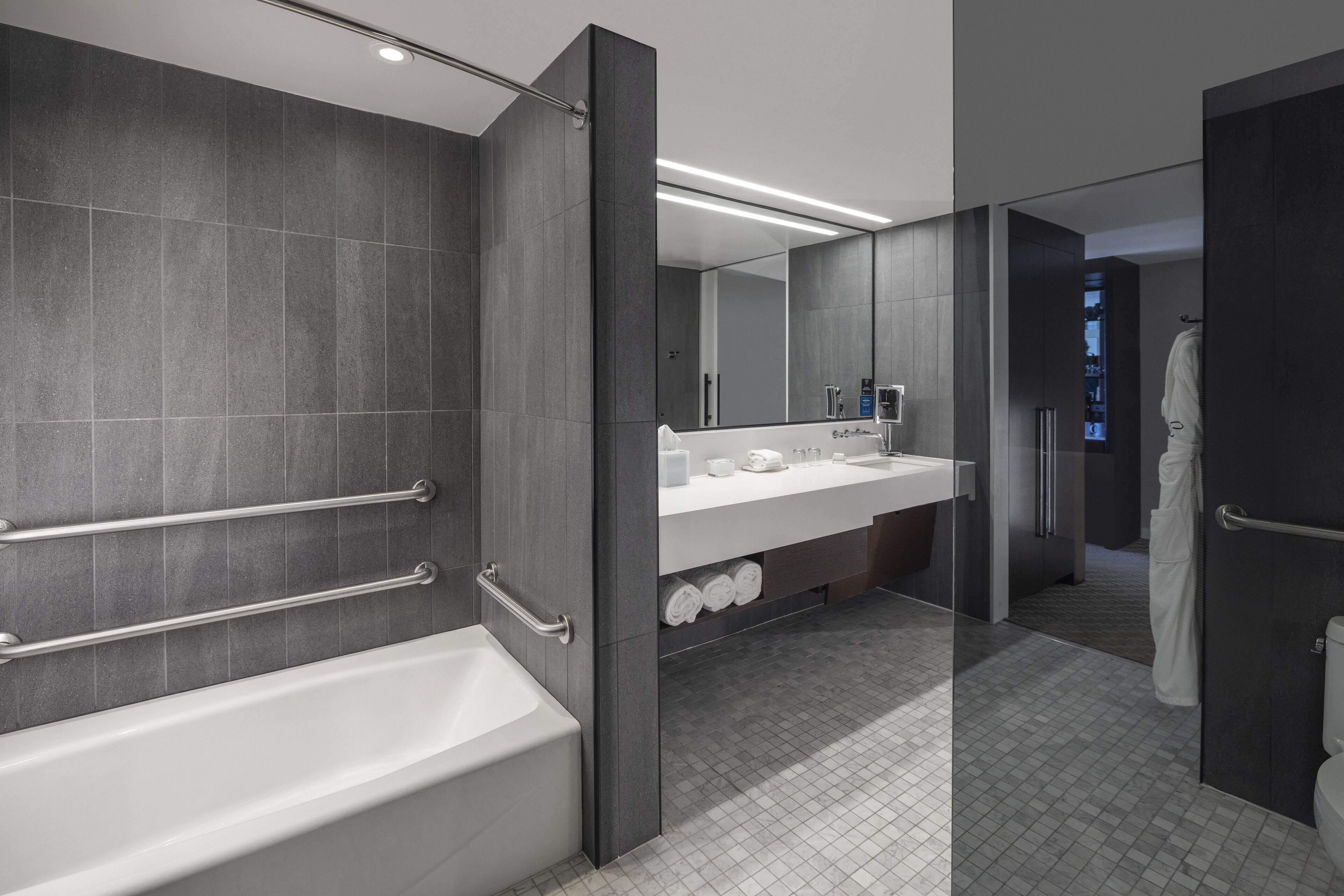 A modern bathroom with a bathtub, a large mirror, and a vanity with a sink and towel storage.
