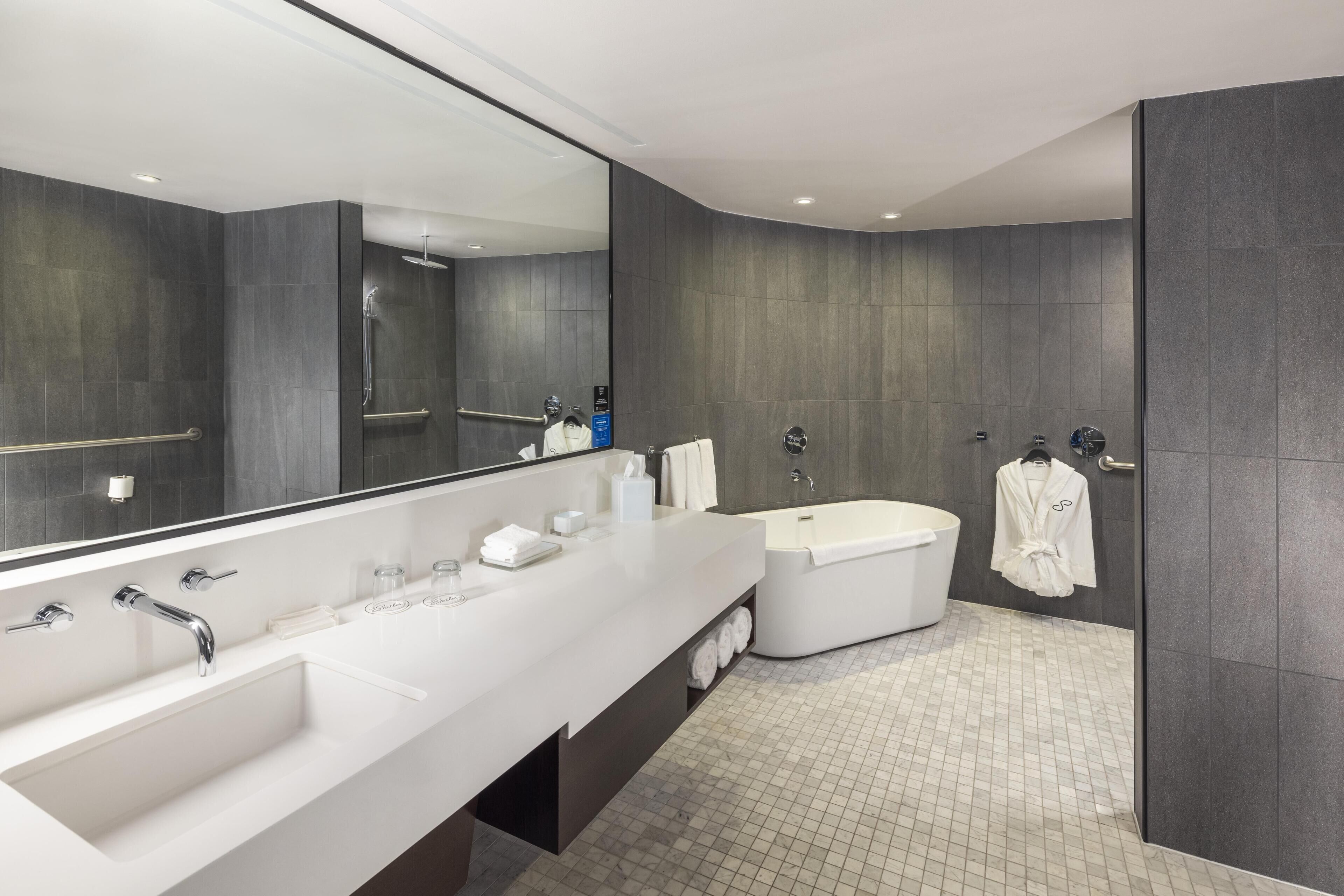 A modern bathroom with a large mirror, a double sink, a bathtub, and a walk-in shower.