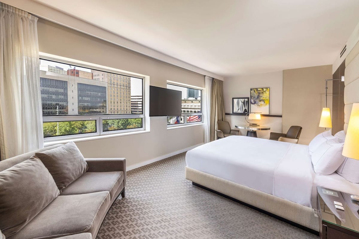 A hotel room with a large bed, a sofa, a TV, and a city view.