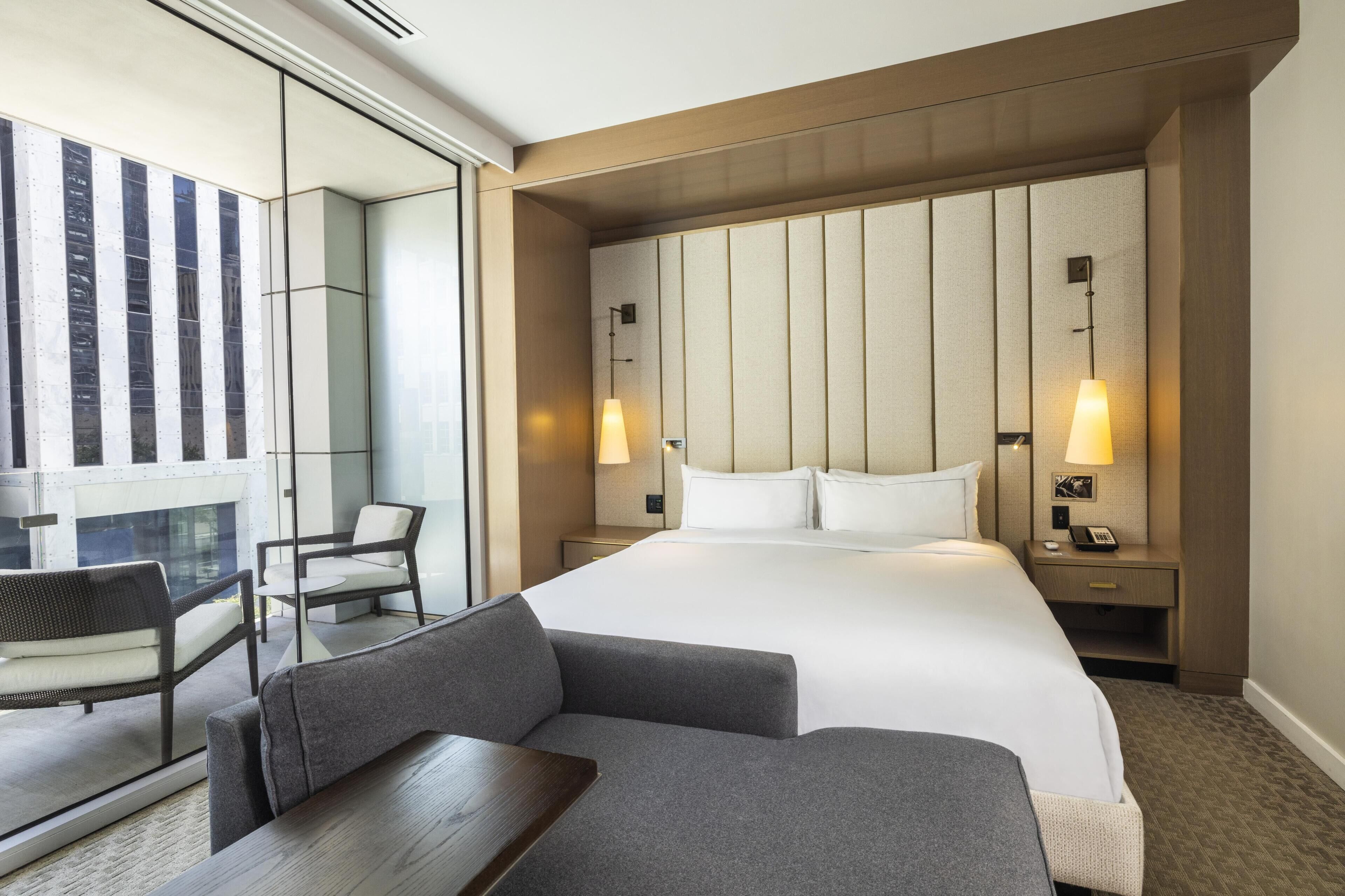 A hotel room with a large bed, two bedside tables, a desk, a chair, and a sofa.