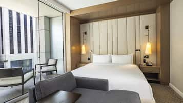 A hotel room with a large bed, two bedside tables, a desk, a chair, and a sofa.