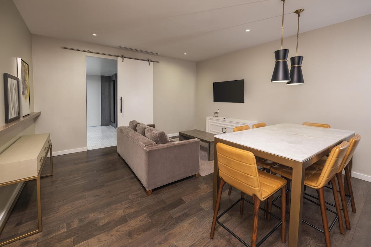 A modern living space with a dining area, sofa, and a flat-screen TV mounted on the wall.