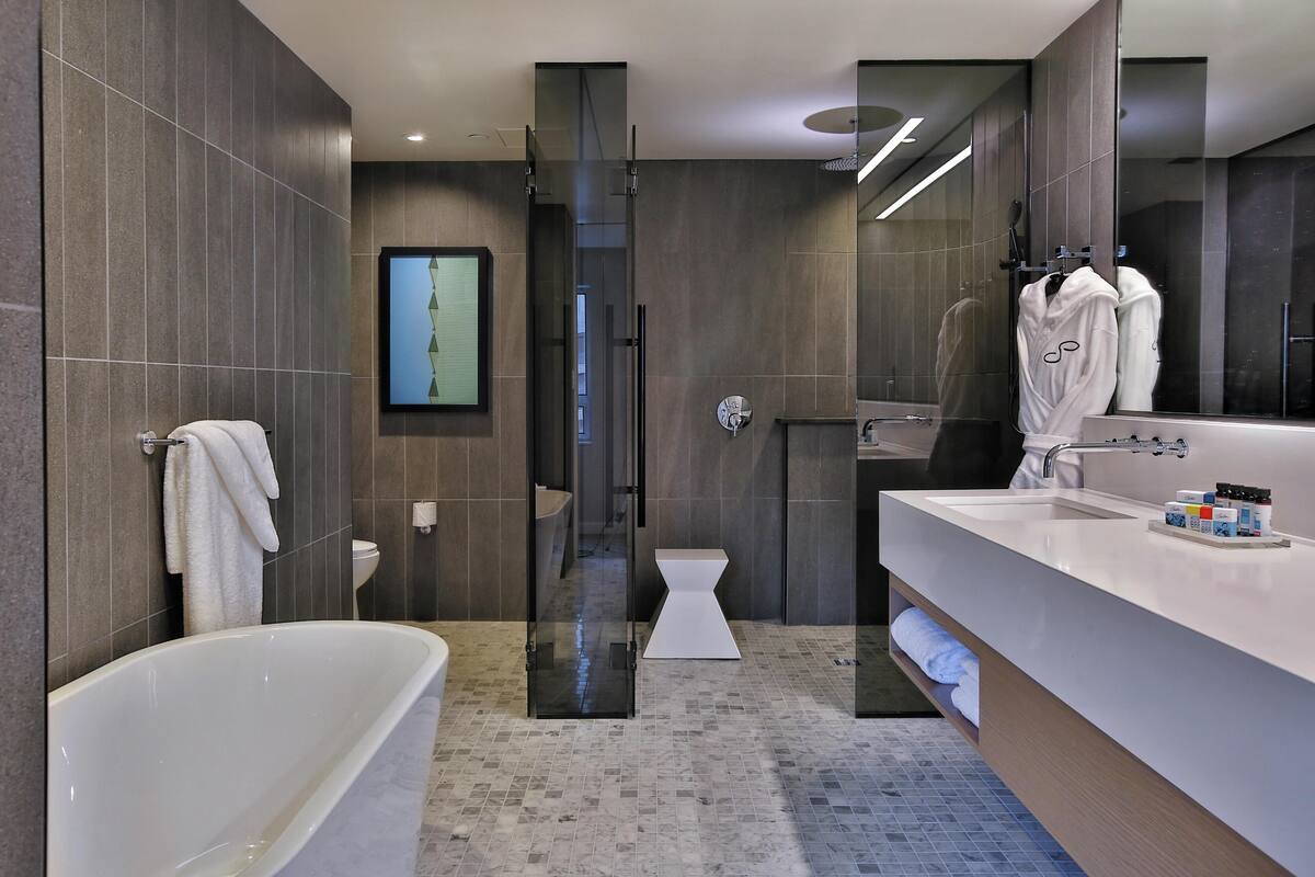 A modern bathroom with a bathtub, a glass-enclosed shower, a toilet, and a large mirror.