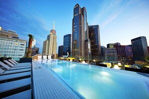 A rooftop infinity pool with city skyline views, modern architecture, and lounge chairs.