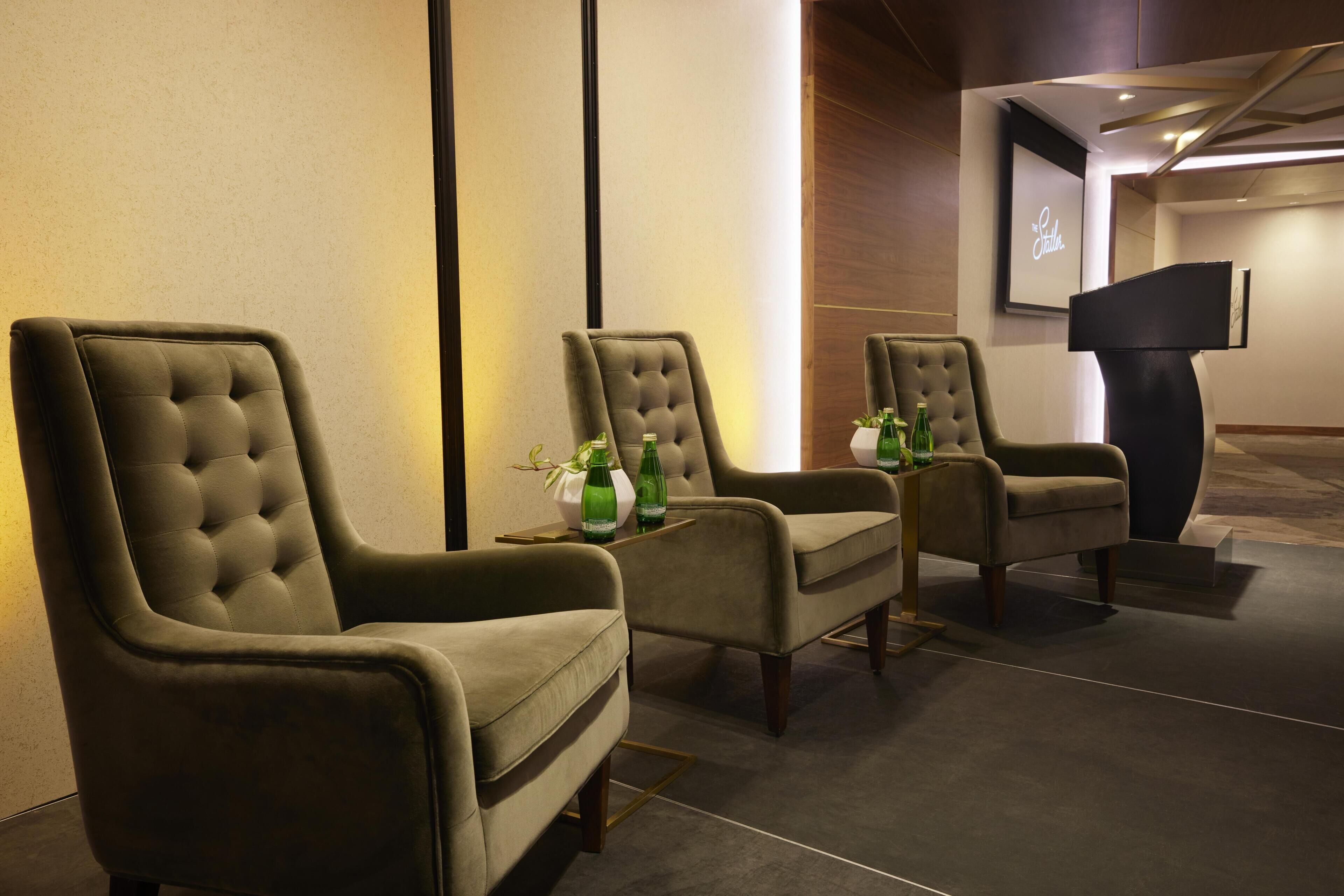 A seating area with three upholstered chairs, a small table with green bottles, and a black podium.