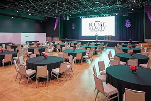 A conference room with multiple round tables, chairs, and a stage with a presentation screen.