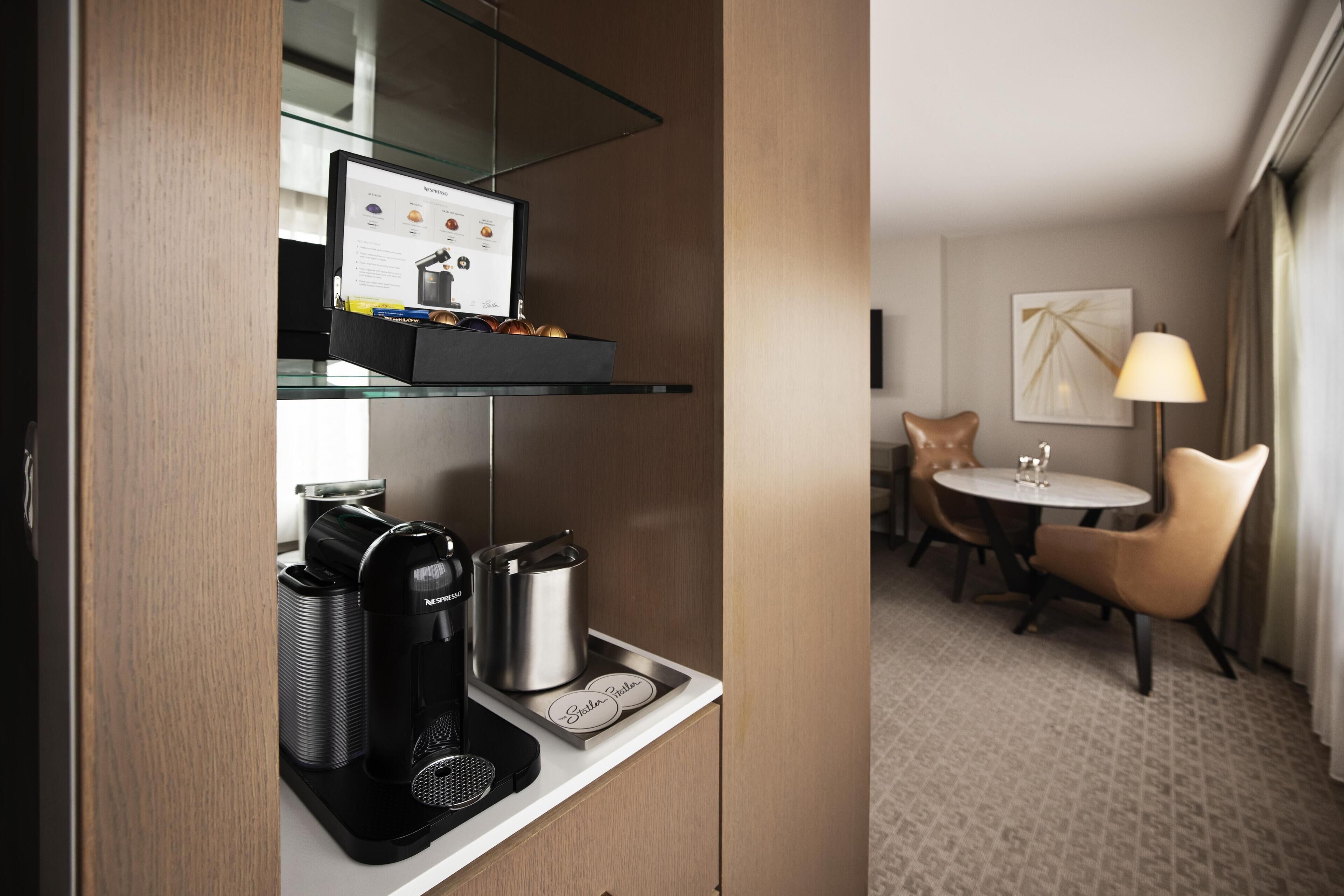 A hotel room with a kitchenette, a dining area with a table and chairs, and a lamp.