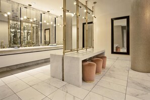 A modern bathroom with a large mirror, multiple lights, a marble countertop, and a bench.