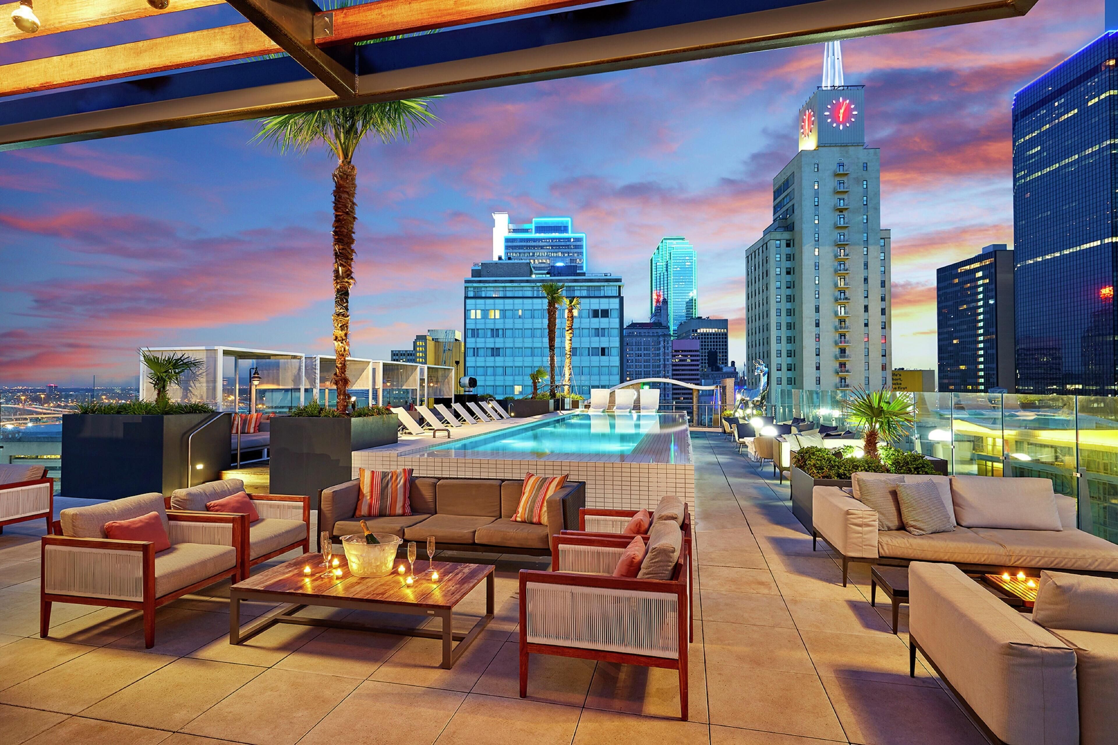A rooftop lounge with a pool, seating, and a city skyline view.