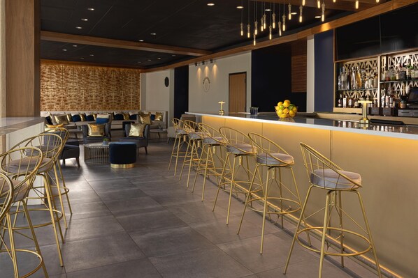 A bar area with high stools, a counter, and a seating area with sofas and chairs.