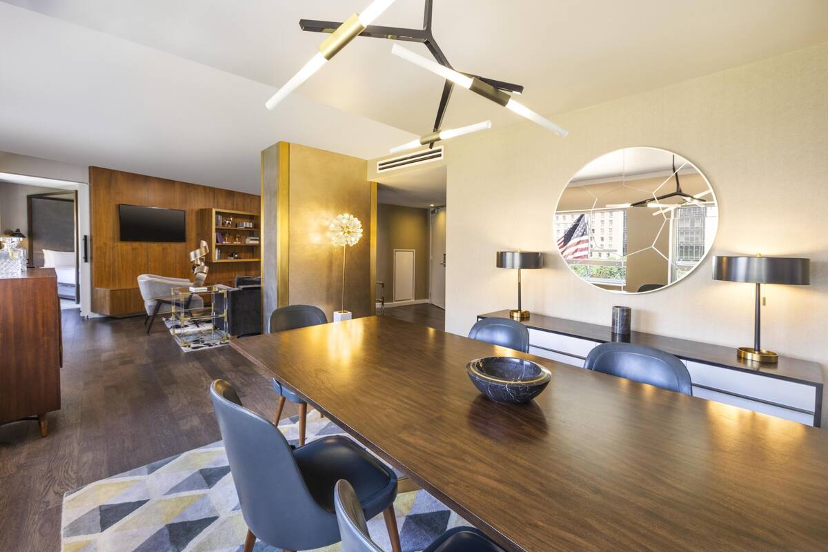 A modern dining area with a wooden table, chairs, a large mirror, and a ceiling light fixture.