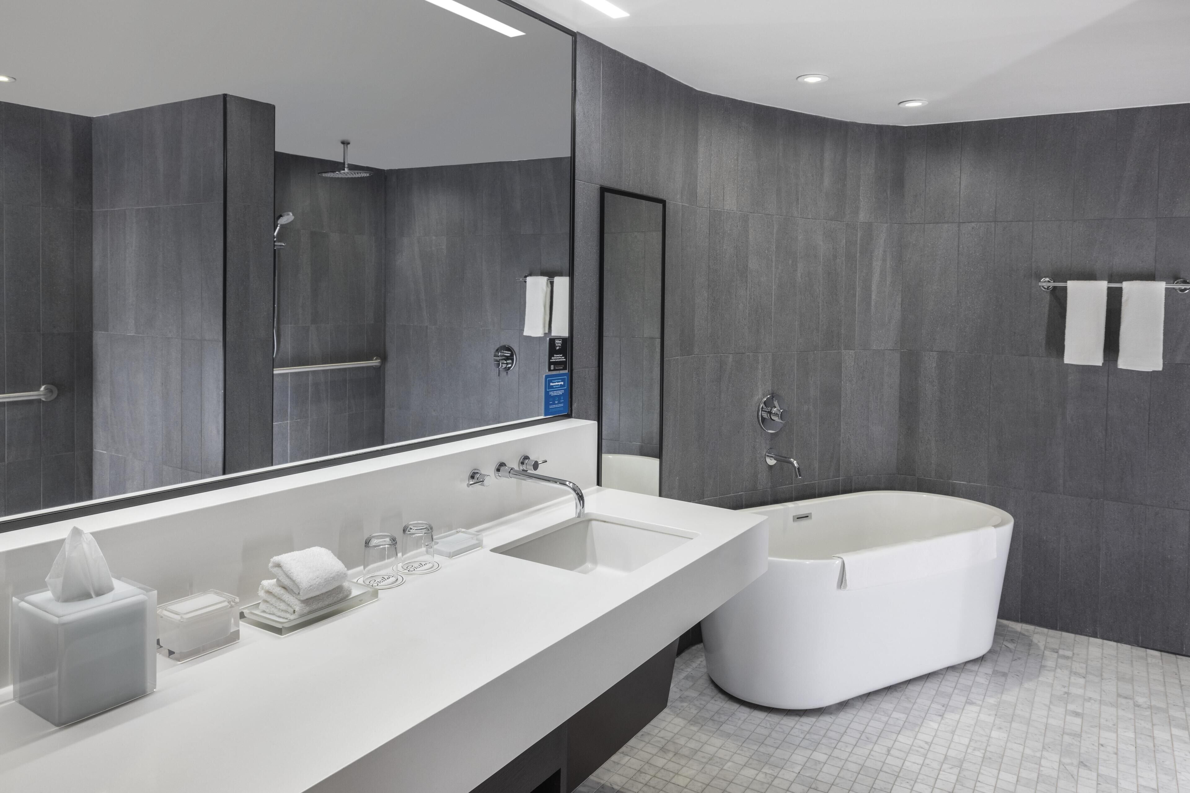 Ein modernes Badezimmer mit großem Spiegel, Waschbecken in Weiß, einer Badewanne und Fliesenboden.