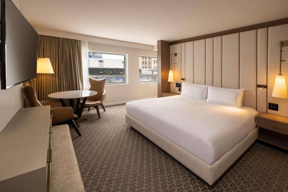 A hotel room with a bed, a desk, a chair, a TV, and a window with curtains.