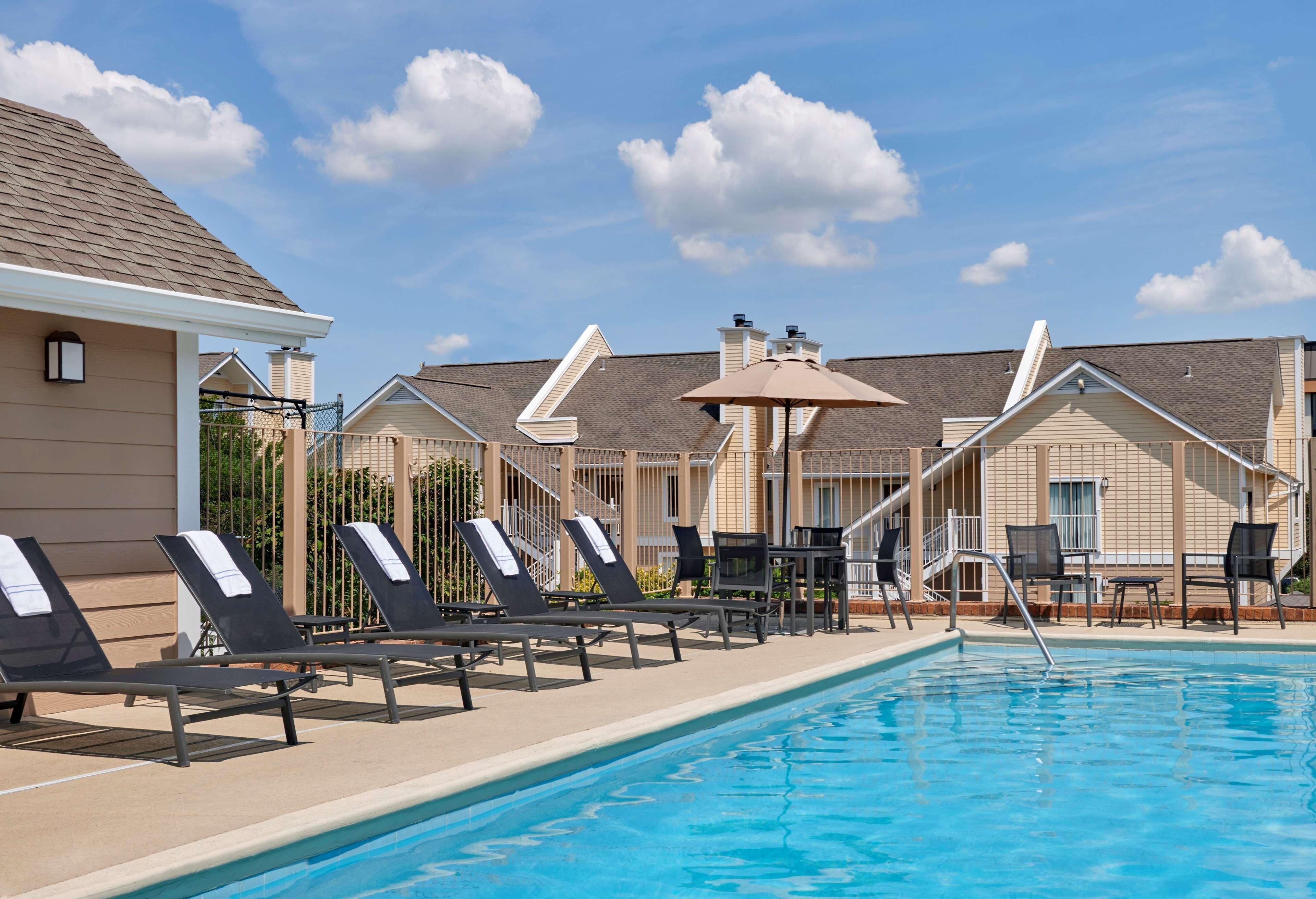 A swimming pool with lounge chairs and umbrellas, surrounded by buildings with a uniform architectural style.