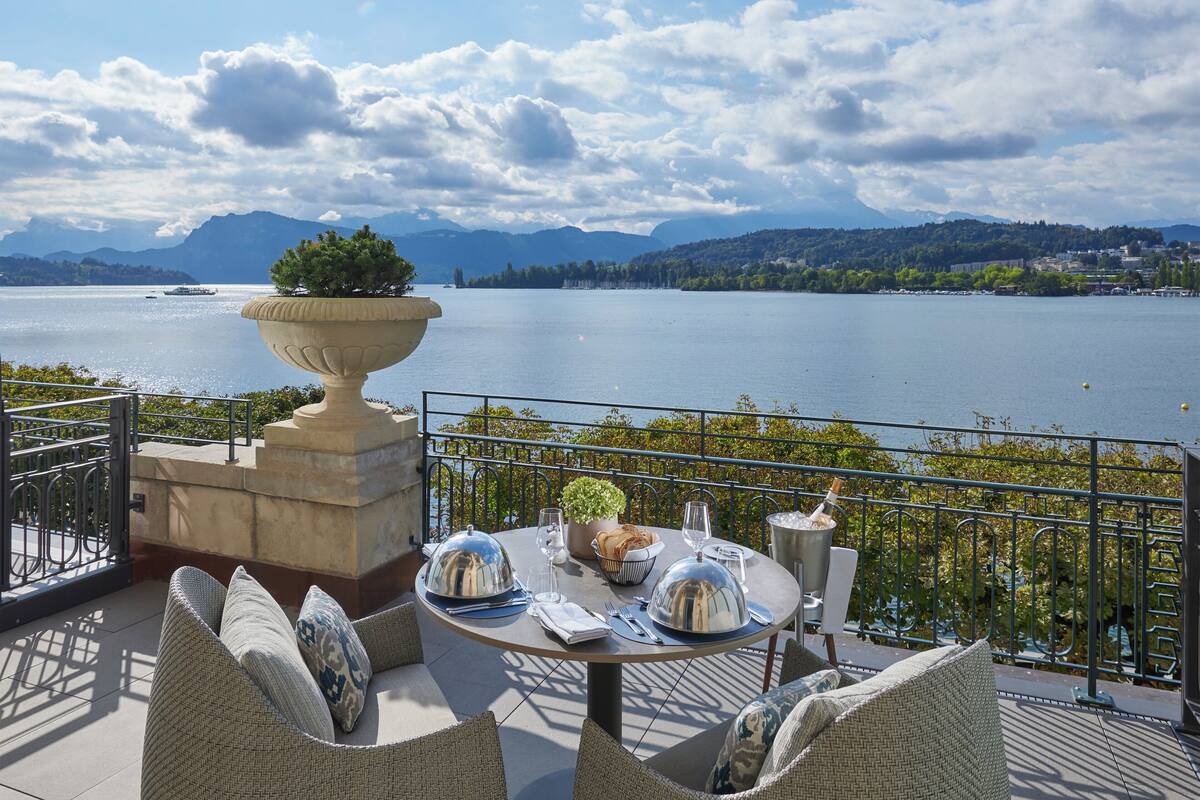 A terrace with a table set for dining, overlooking a lake with mountains in the background.