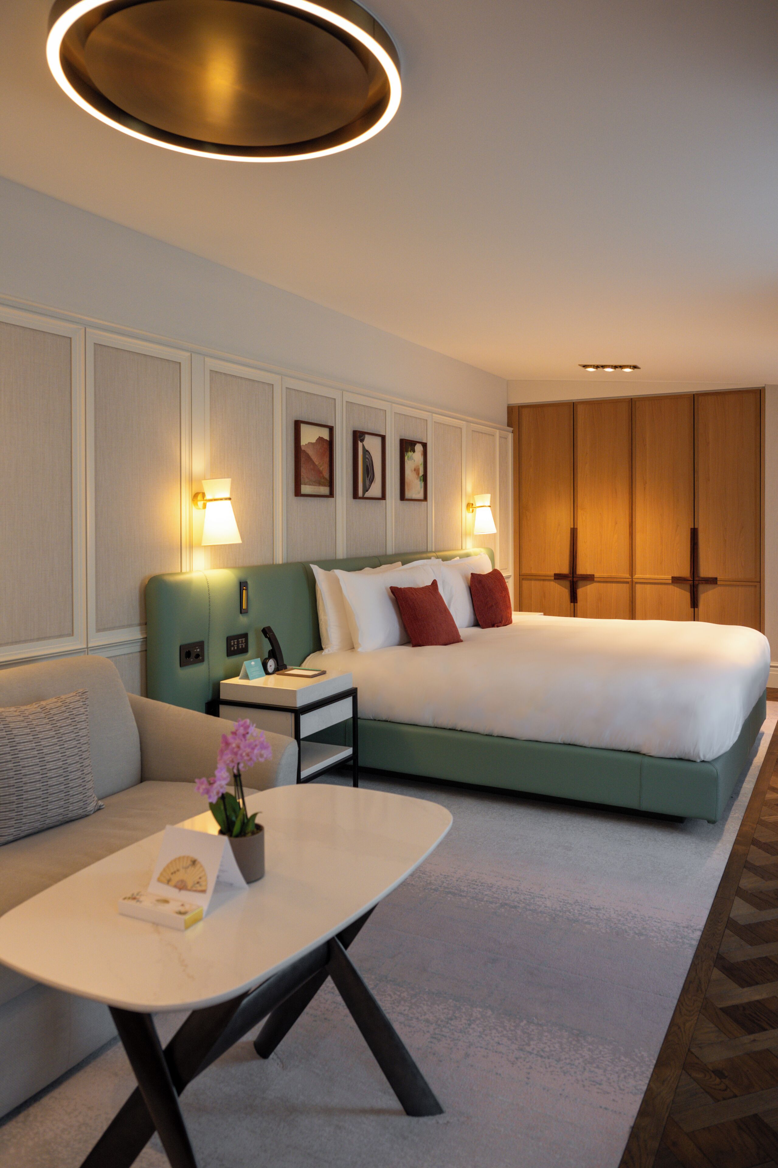A hotel room with a bed, bedside tables, a sofa, a coffee table, and a wall-mounted lamp.