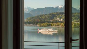 A view through a door of a lake with a boat, mountains in the background, and a balcony with a metal railing.