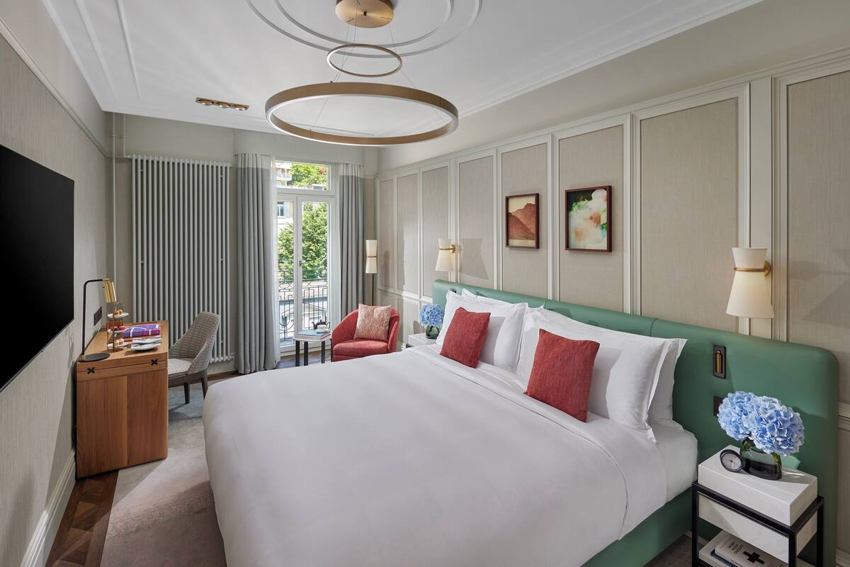 A hotel room with a large bed, a TV, a desk, and a chair.