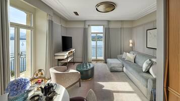 Ett rymligt hotellrum med ett stort fönster som erbjuder utsikt över vattnet, en soffa, en matplats med ett bord för två personer och en tv.