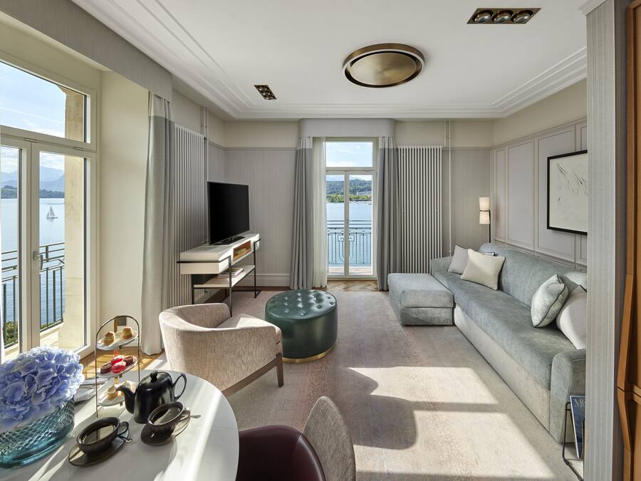 Ett rymligt hotellrum med ett stort fönster som erbjuder utsikt över vattnet, en soffa, en matplats med ett bord för två personer och en tv.