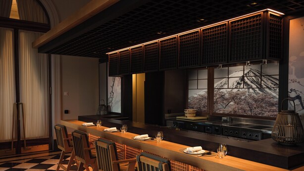 A modern kitchen with a long counter, bar stools, and a large window with a view of cherry blossoms. - Mandarin Oriental Palace, Luzern (Lucerne)