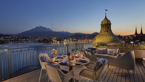A terrace with a table set for dining, overlooking a body of water and a cityscape with mountains in the background. - Mandarin Oriental Palace, Luzern (Lucerne)