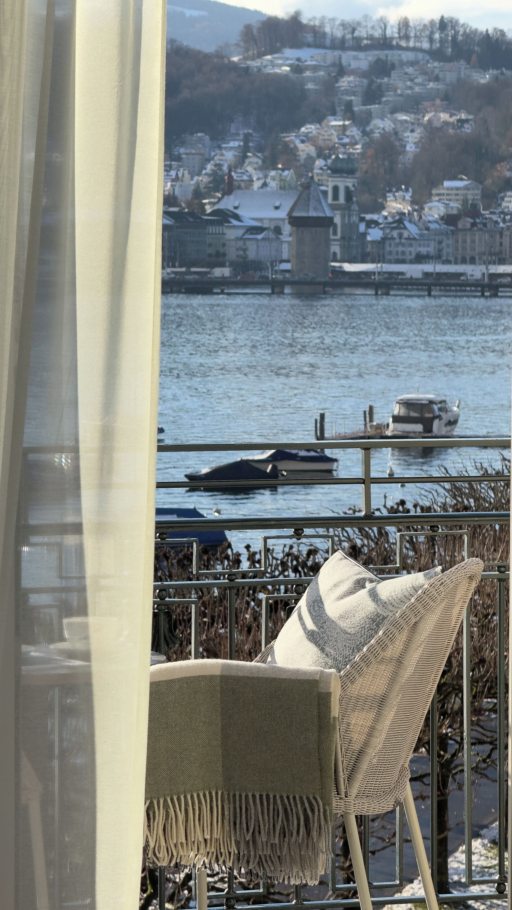A view from a balcony with a chair and a table, overlooking a river with boats and buildings in the background.