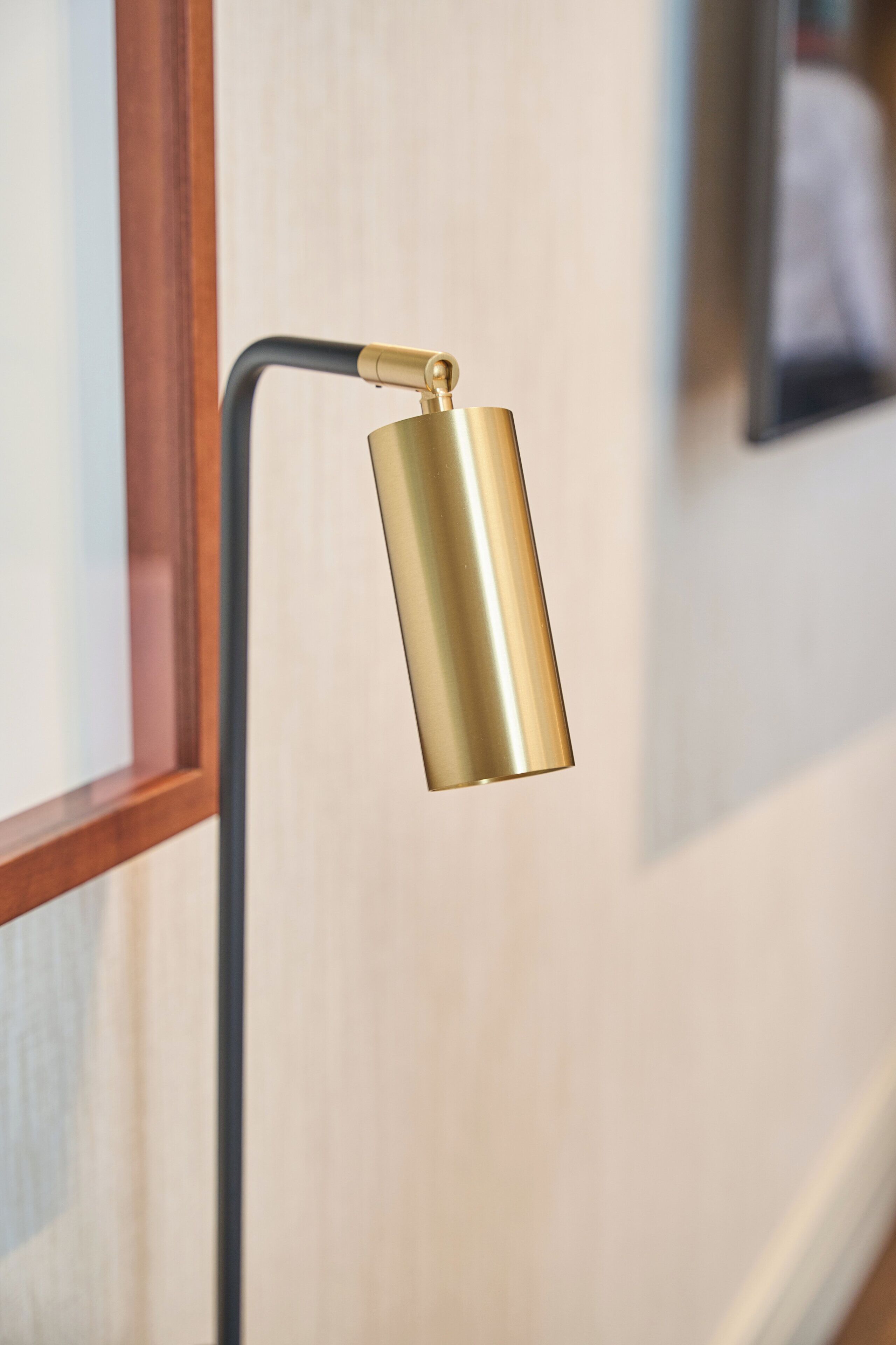 A modern floor lamp with a curved arm and a cylindrical shade, positioned near a window with a wooden frame.