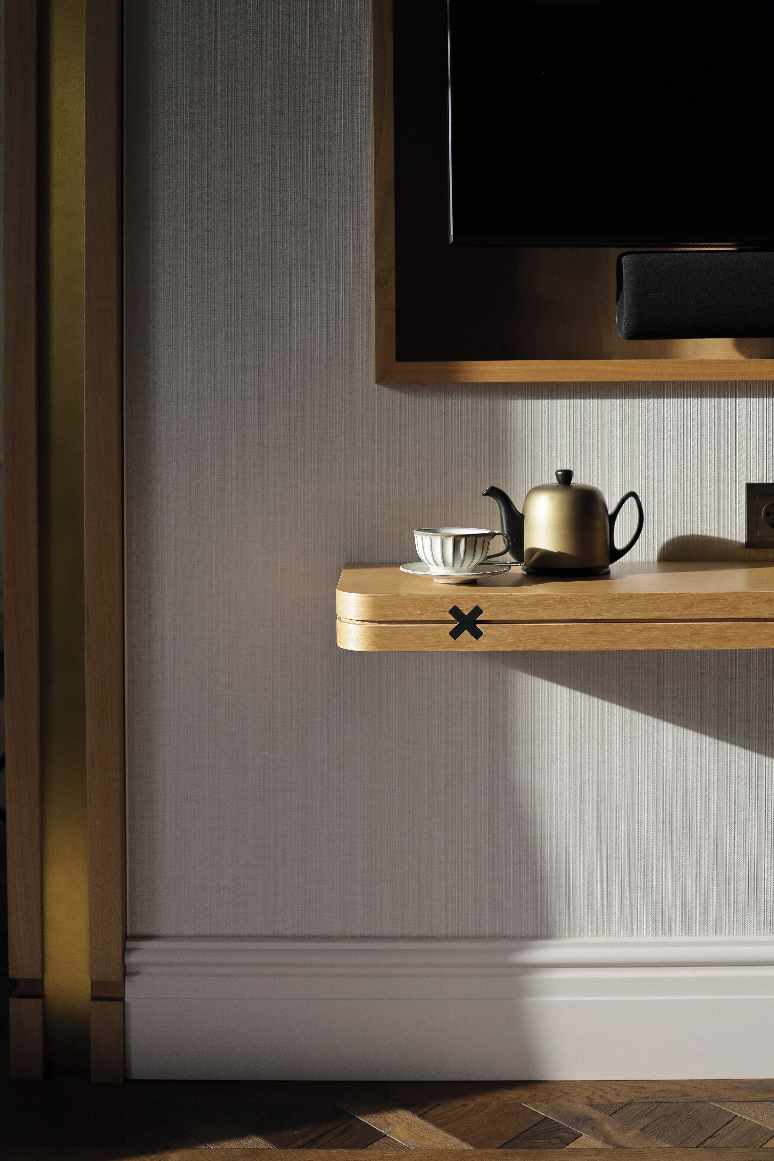A wooden shelf with a teapot and cup, a television mounted above, and a textured wall.