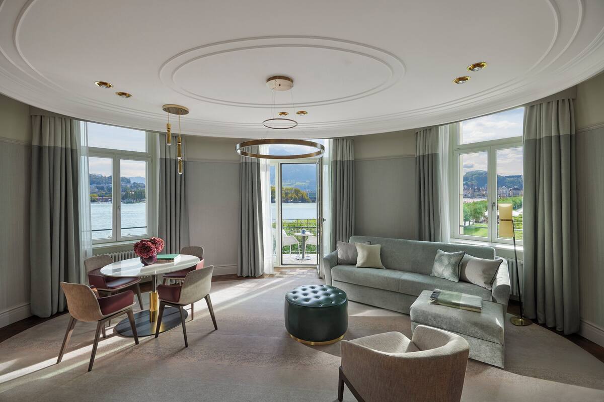 A spacious living room with a view of a lake, a round dining table with chairs, a sofa, and a coffee table.