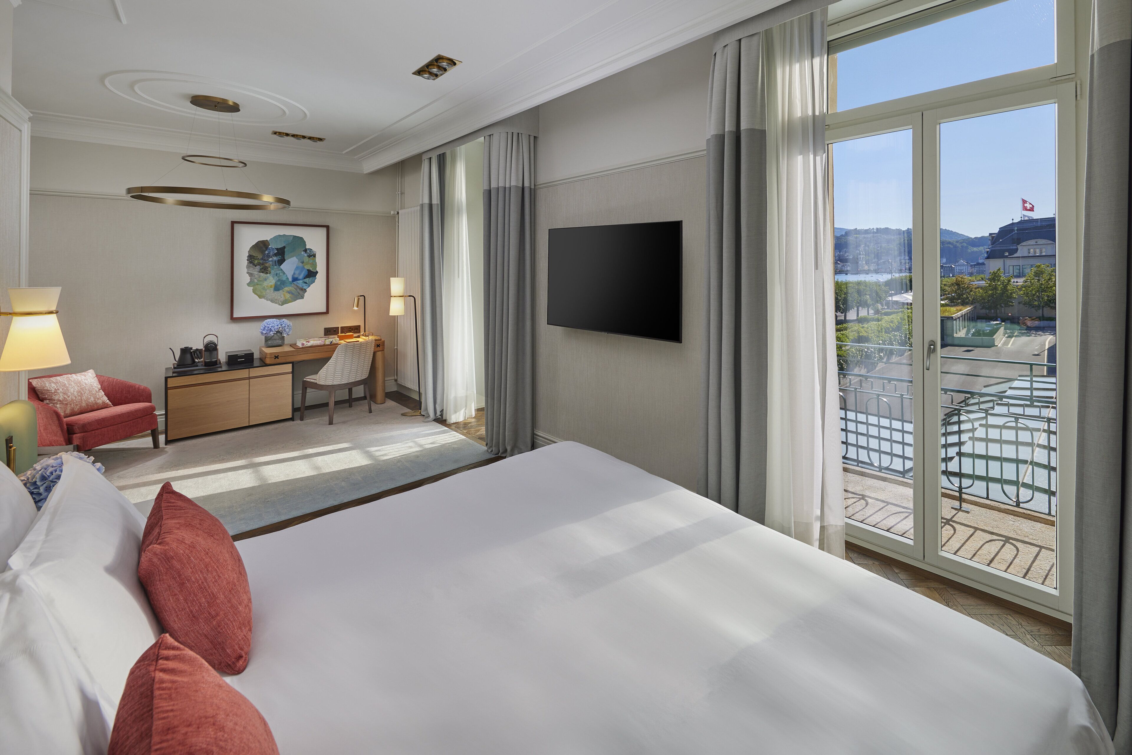A hotel room with a large bed, a desk, a chair, a TV, and a balcony with a view of the city.