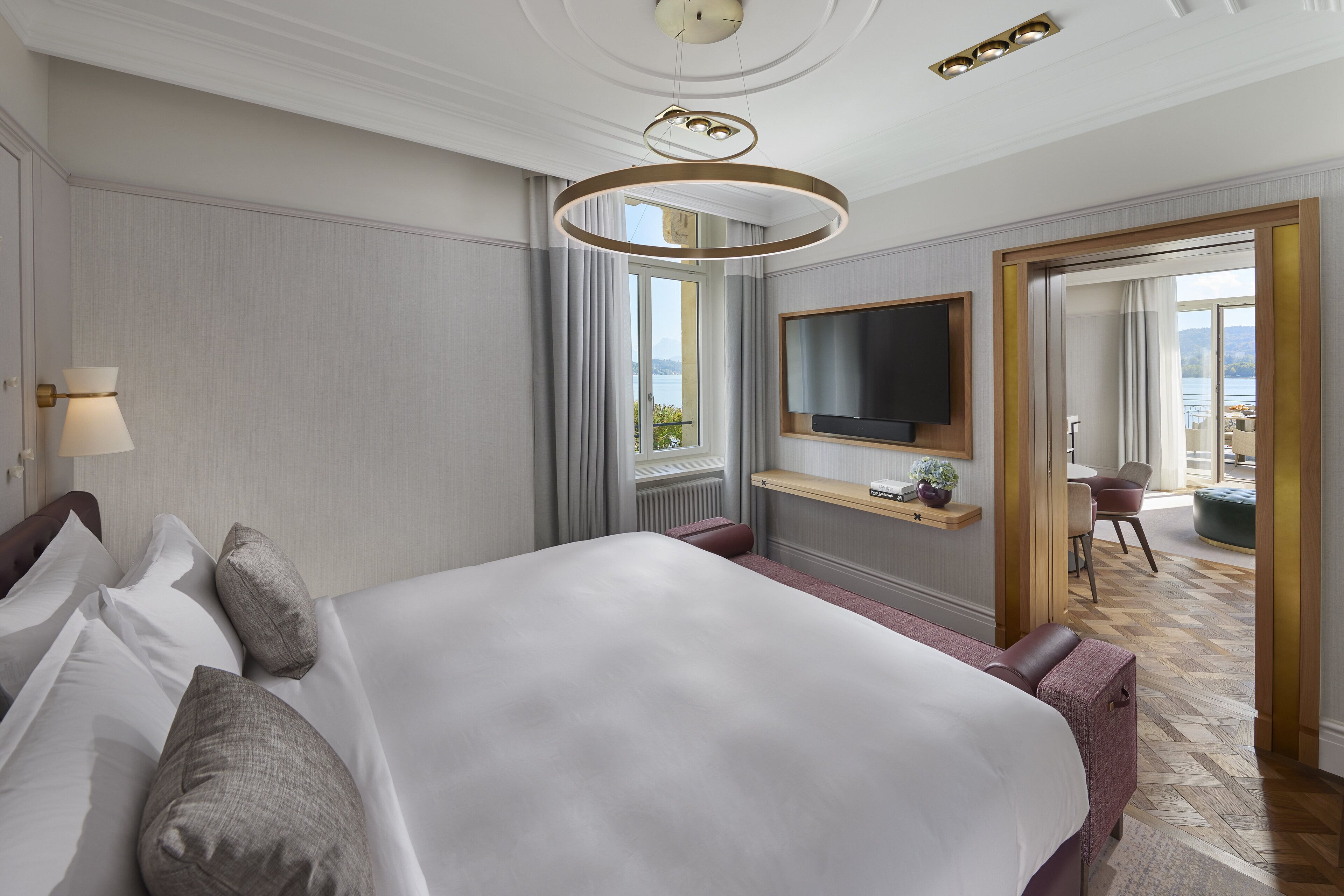 Habitación de hotel con una cama grande, un televisor montado en la pared, una ventana con cortinas y vistas al exterior.