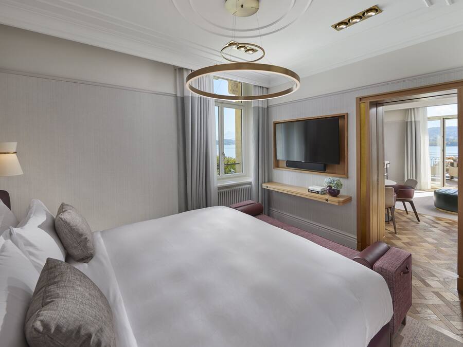 Habitación de hotel con una cama grande, un televisor montado en la pared, una ventana con cortinas y vistas al exterior.