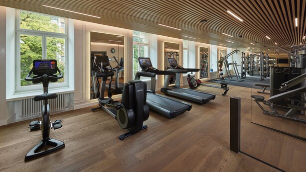 A modern gym with cardio machines, weight training equipment, and large windows.