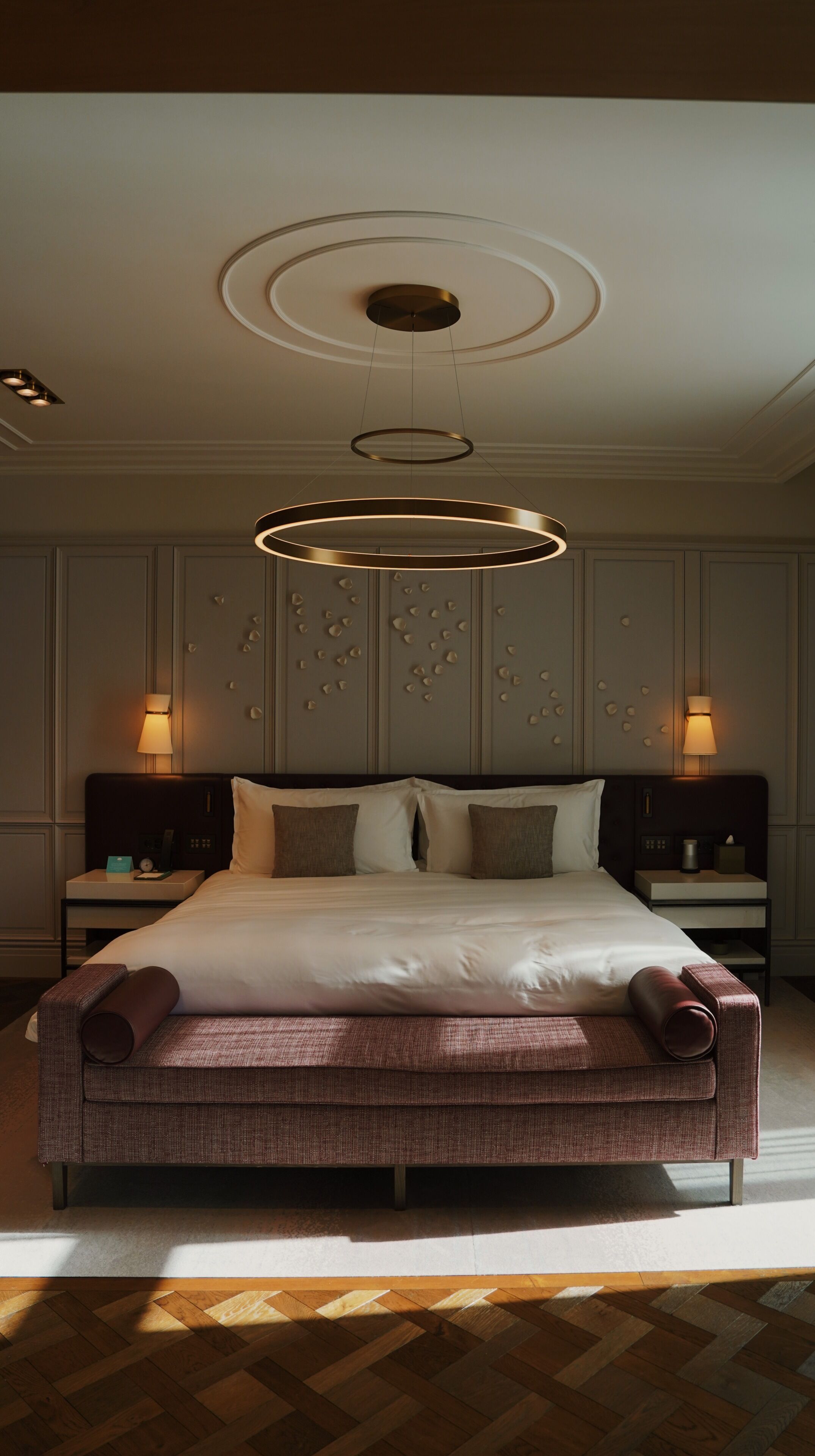A modern hotel room with a large bed, two bedside tables, a wall-mounted lamp, and a circular ceiling light fixture.