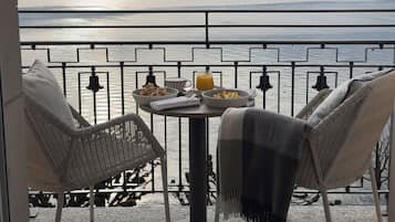 Ein Balkon mit Tisch, zwei Korbstühlen und Blick auf einen See und Berge.