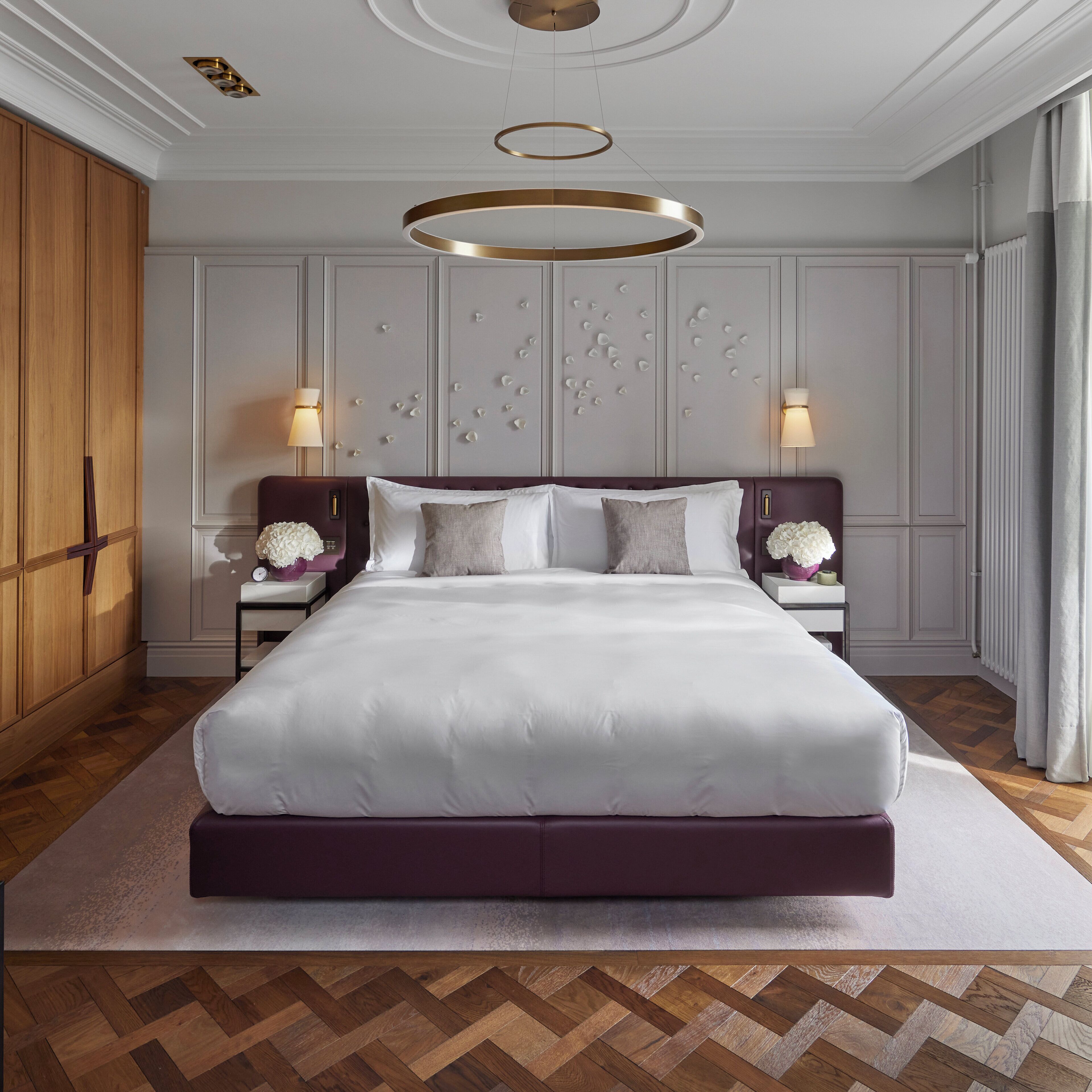 Una cama grande con cabecera, dos mesitas de noche con lámparas, una pared decorativa y un armario de madera.