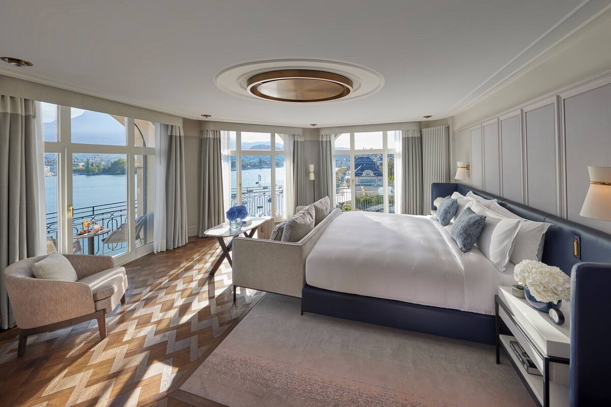 A spacious bedroom with a large bed, a seating area, and a view of a body of water.