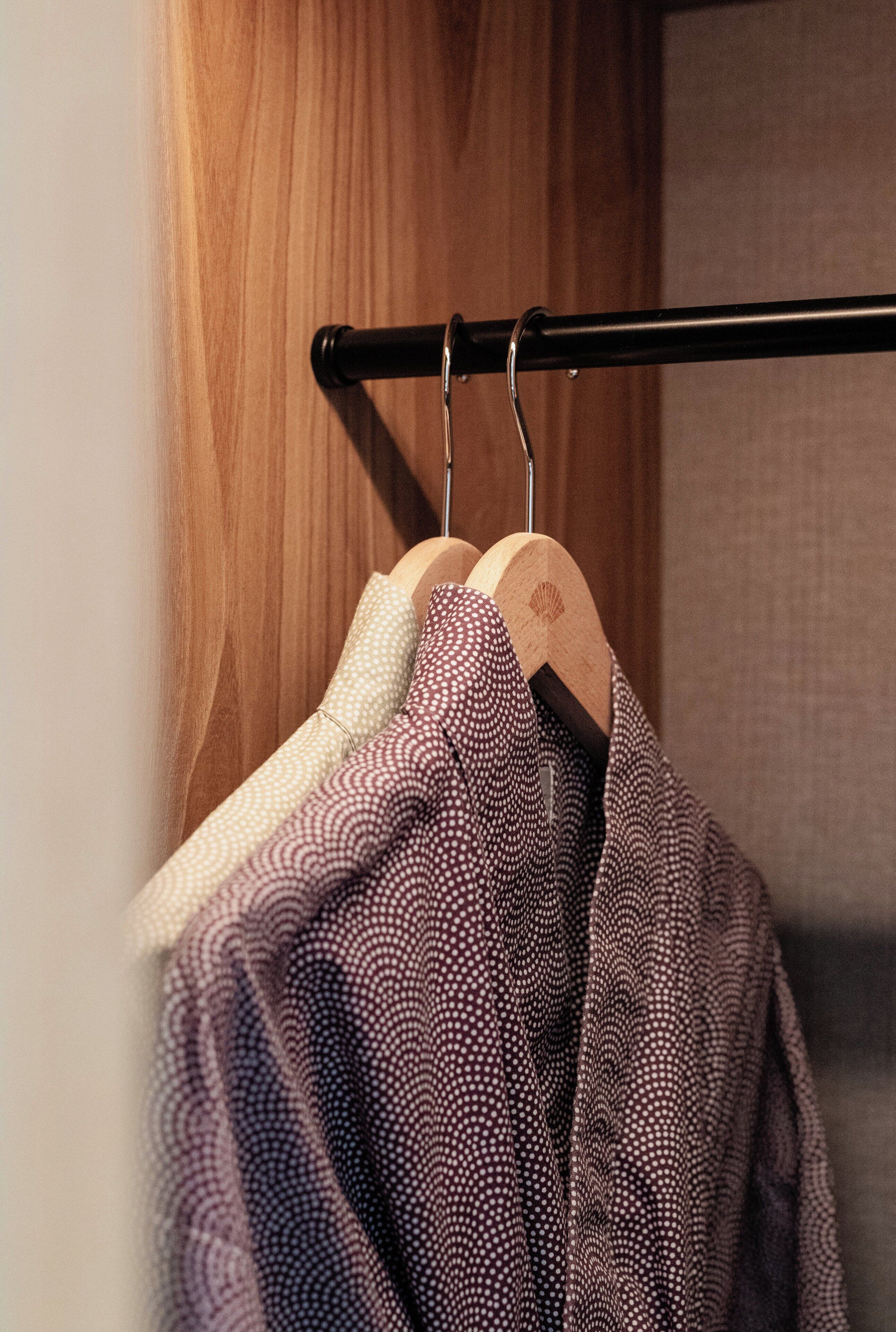 A wooden wardrobe with a black metal rod holding a white and a patterned garment.