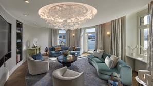 Un salon spacieux agrémenté d’un lustre moderne, d’un grand ensemble de canapés et offrant une vue sur l’extérieur grâce à de grandes fenêtres.