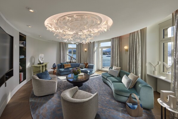 A spacious living room with a modern chandelier, a large sofa set, and a view of the outdoors through large windows. - Mandarin Oriental Palace, Luzern (Lucerne)