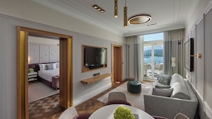 Une chambre d’hôtel moderne dotée d’un grand lit, d’un téléviseur fixé au mur, d’un coin salon avec un canapé et des fauteuils, et offrant une vue sur l’extérieur.