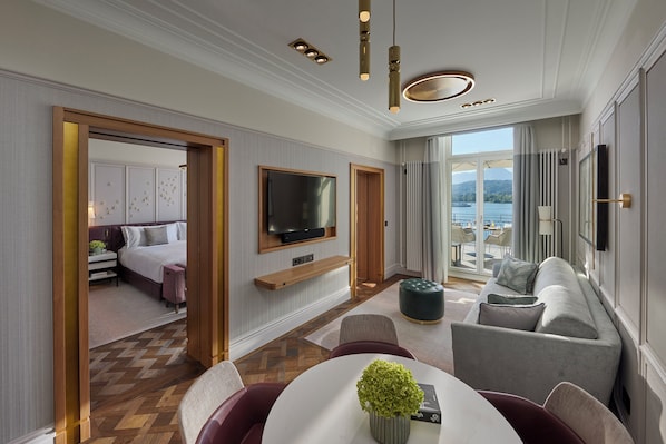 Une chambre d’hôtel moderne dotée d’un grand lit, d’un téléviseur fixé au mur, d’un coin salon avec un canapé et des fauteuils, et offrant une vue sur l’extérieur.