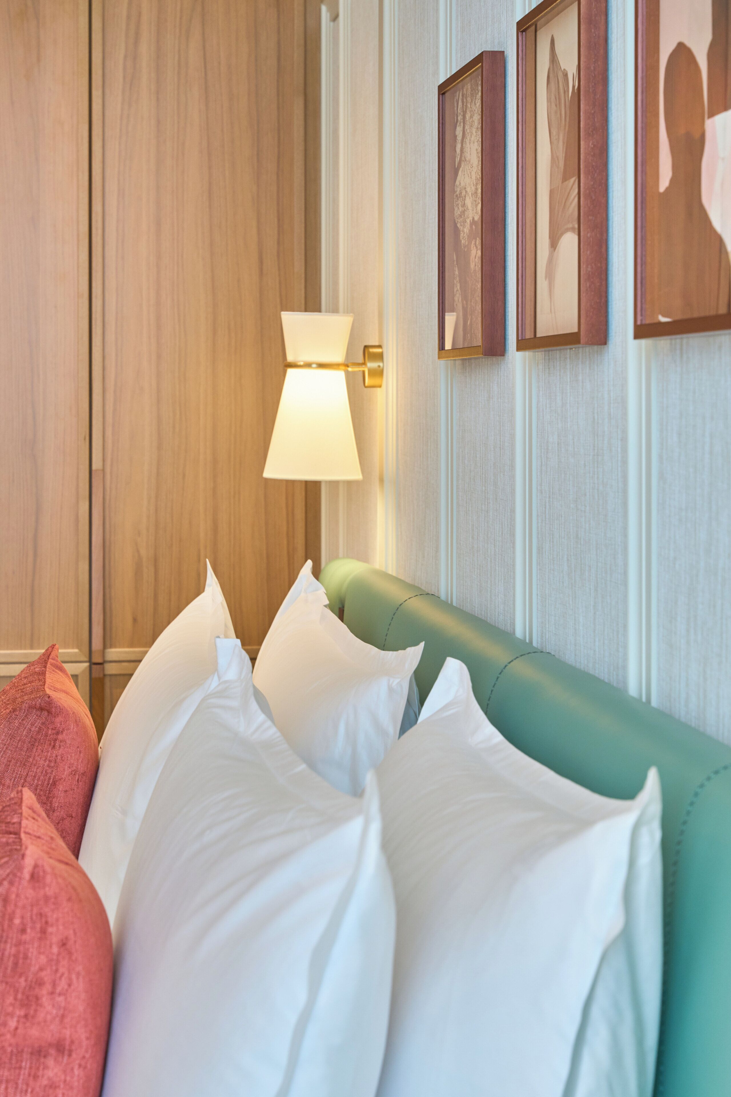 A hotel room with a bed, pillows, a lamp, and framed pictures on the wall.